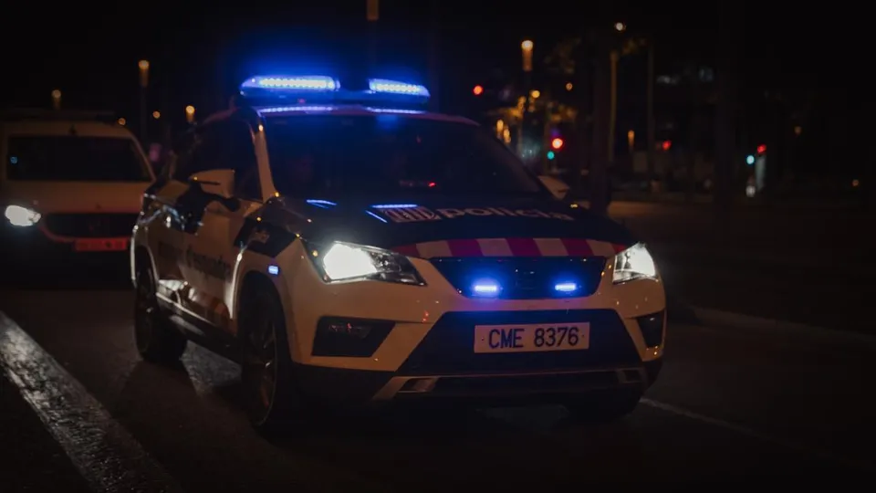 Police car with flashing lights on a Barcelona street at night, possibly during a pursuit or arrest.