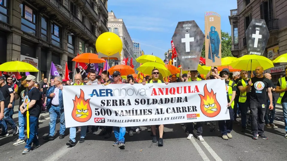 Workers protesting outside a factory building in Barcelona, holding signs about job protection.