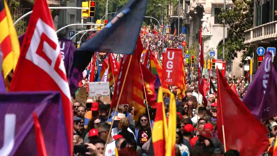 Protesters march through a city street in Barcelona, holding union flags and banners during a May Day demonstration.