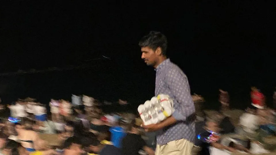 A street vendor selling cans of beer in a busy Barcelona square at night.