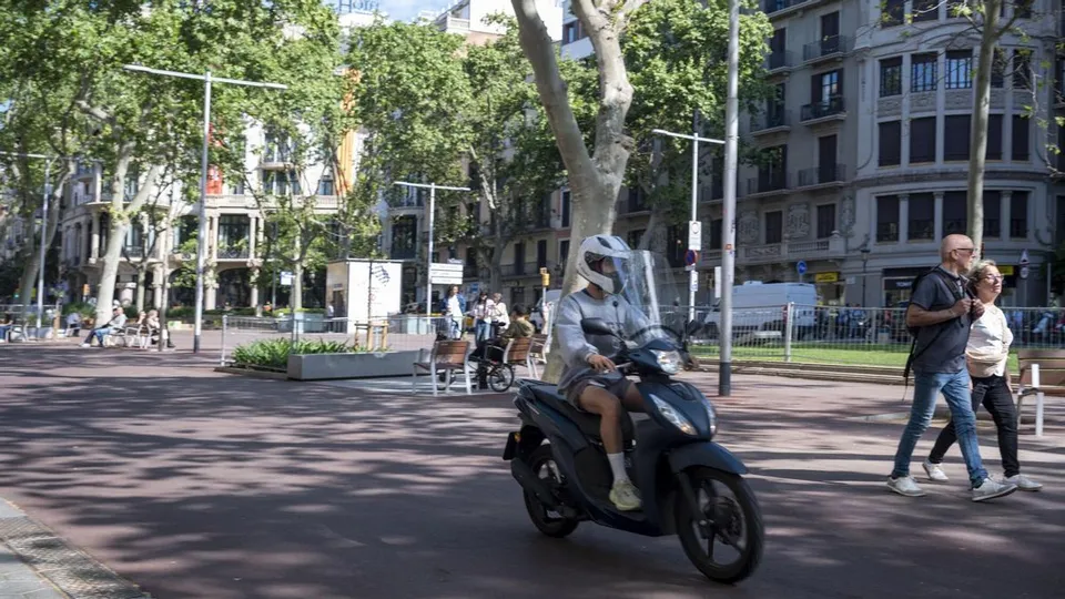 A motorcyclist drives through a pedestrianised section of Jardinets del Passeig de Gràcia in Barcelona, past people walking.