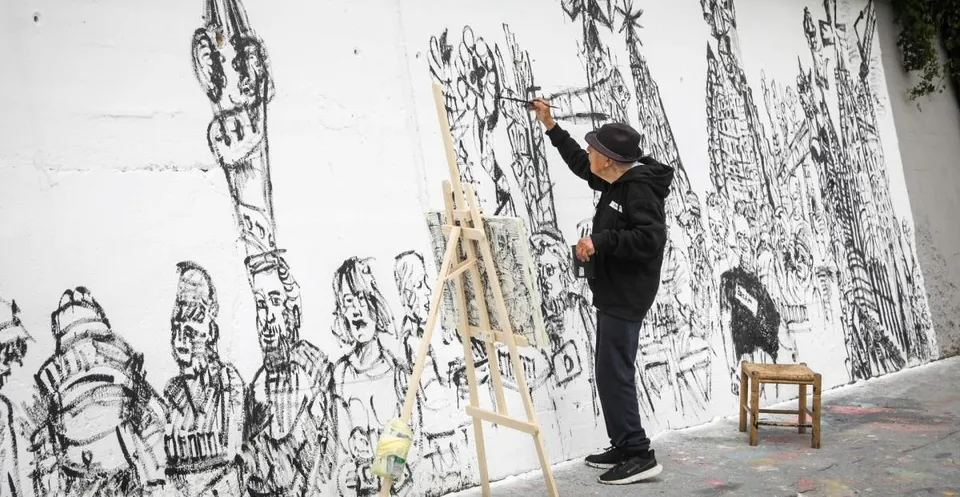 Joan Bueno, a 93-year-old artist, stands proudly next to his newly completed 17-metre mural at BesArt, depicting everyday Bar