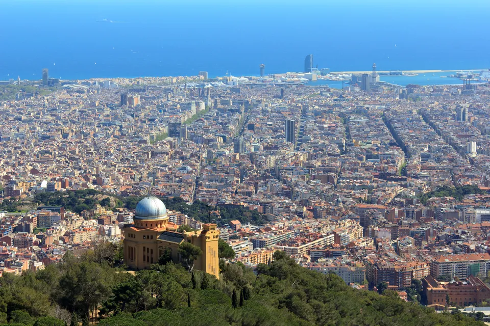 A view of the Fabra Observatory on Montjuïc hill in Barcelona, under a partly cloudy sky, with the city visible below.